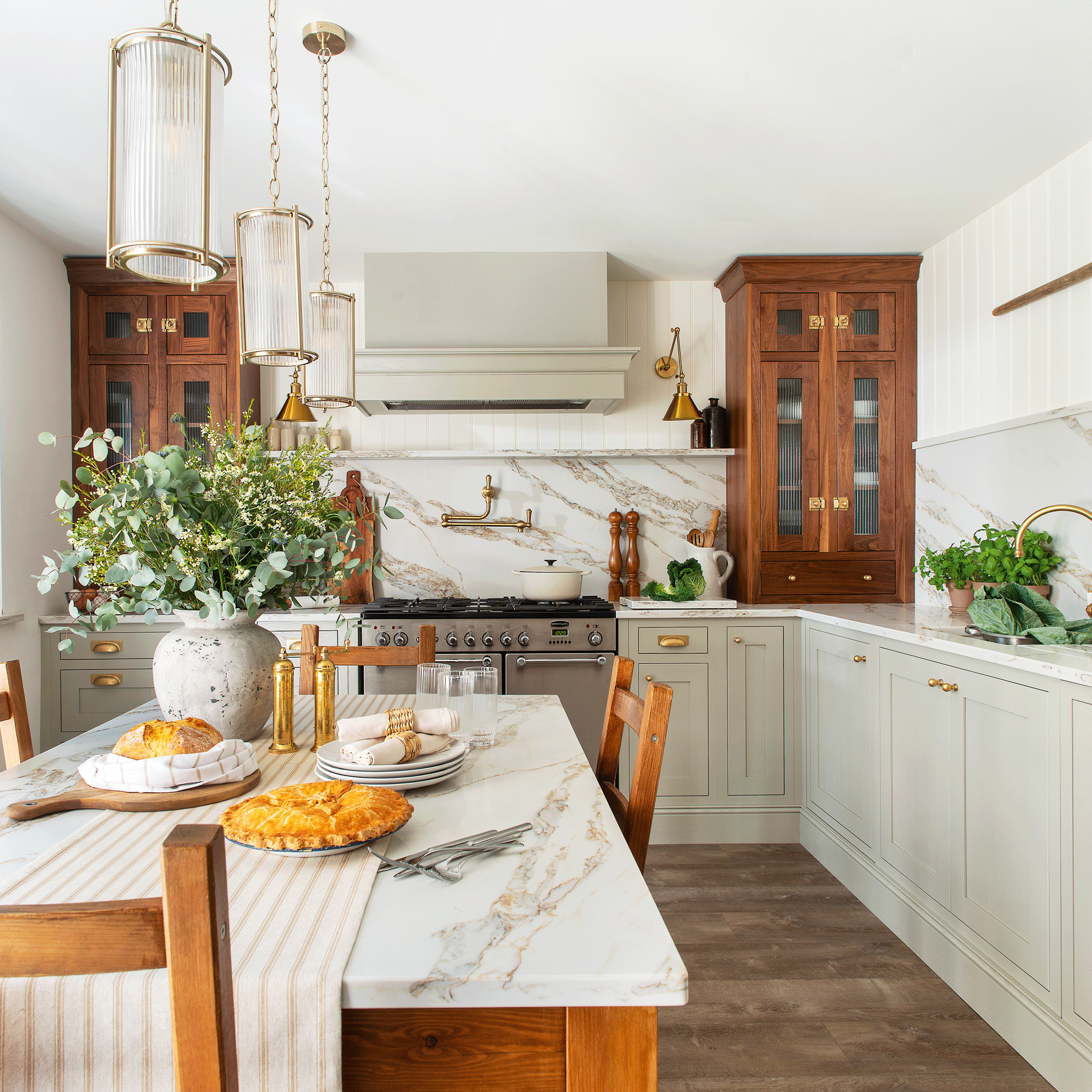 a neutral country-style kitchen with a farmhouse table and chairs in the middle a large range cooker pale green cabinetry and a marble splashback