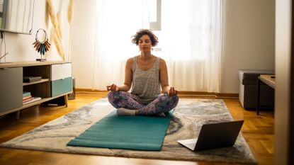 Woman doing meditative yoga pose on a mat in her living room