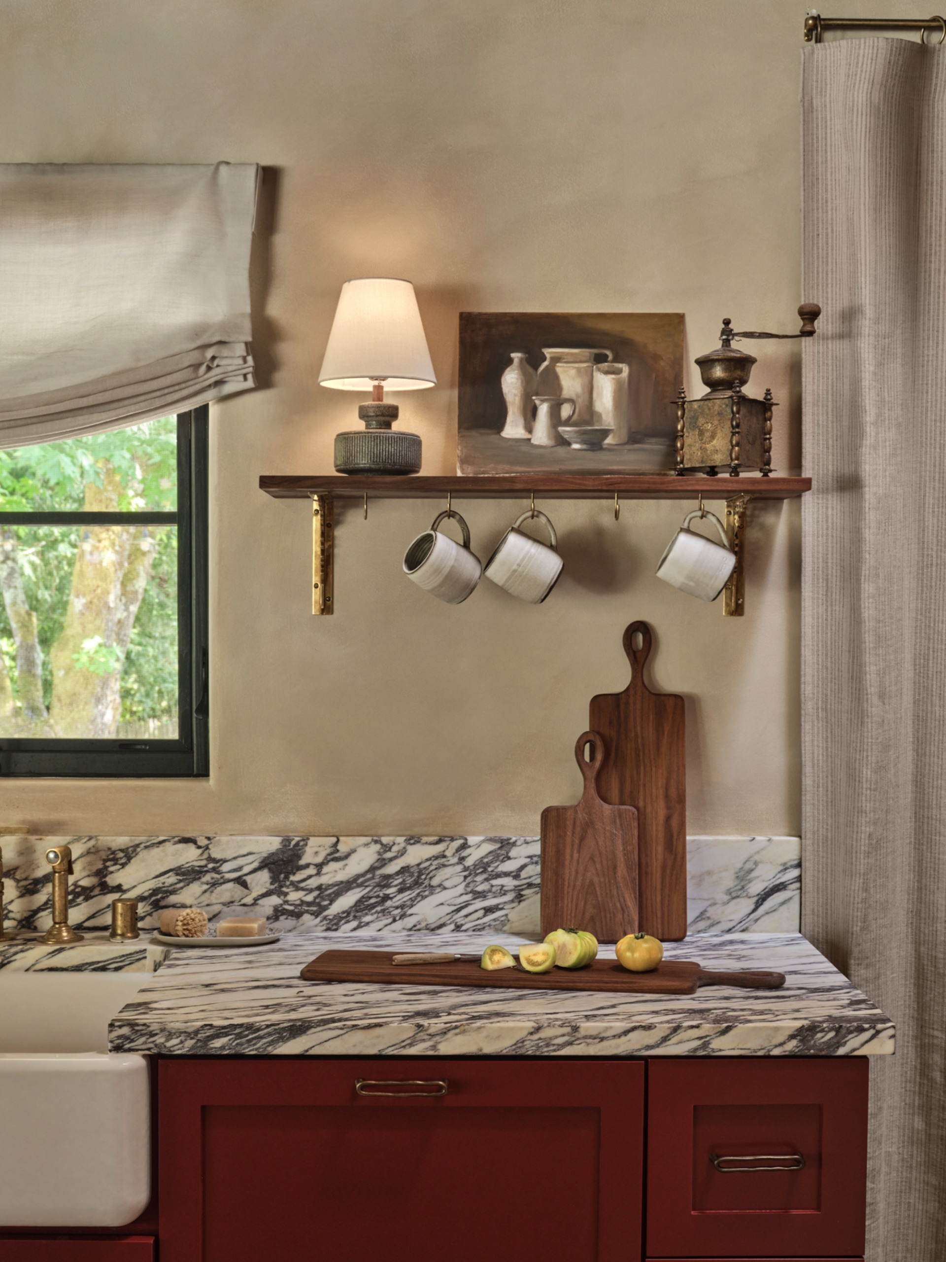 a limewashed kitchen with burgundy cabinetry, a stone bench and timber hanging shelf for objects and mugs