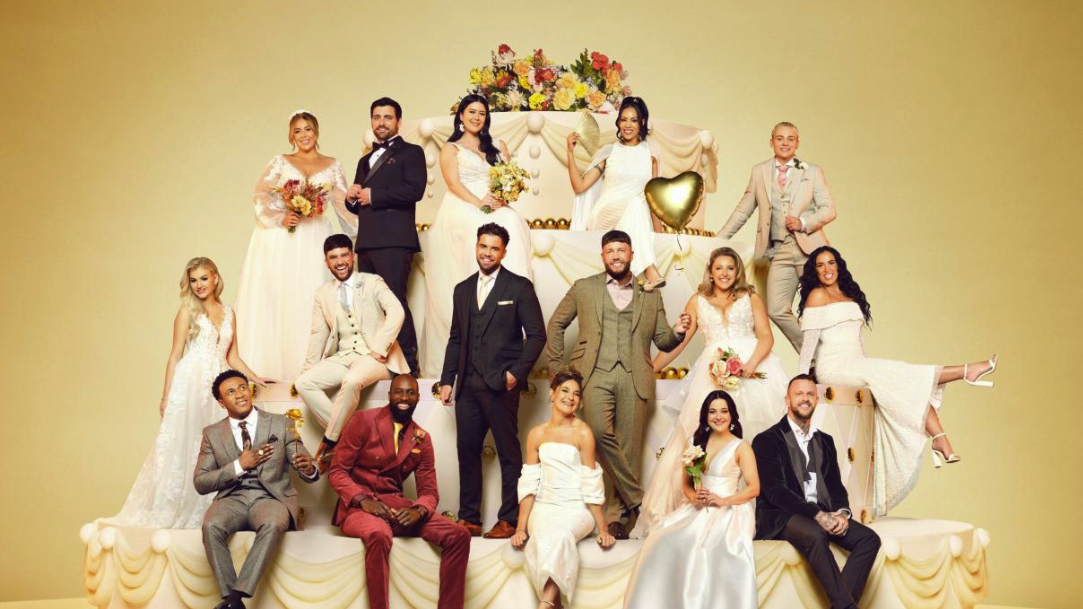 The cast of Channel 4&#039;s Married at First Sight UK season 9 pose in wedding attire around a giant prop wedding cake against a gold background