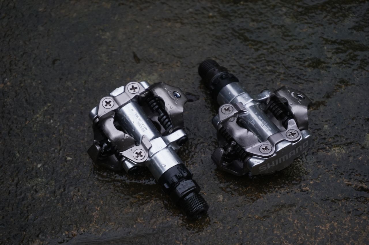 A pair of silver gravel bike pedals on a stone surface