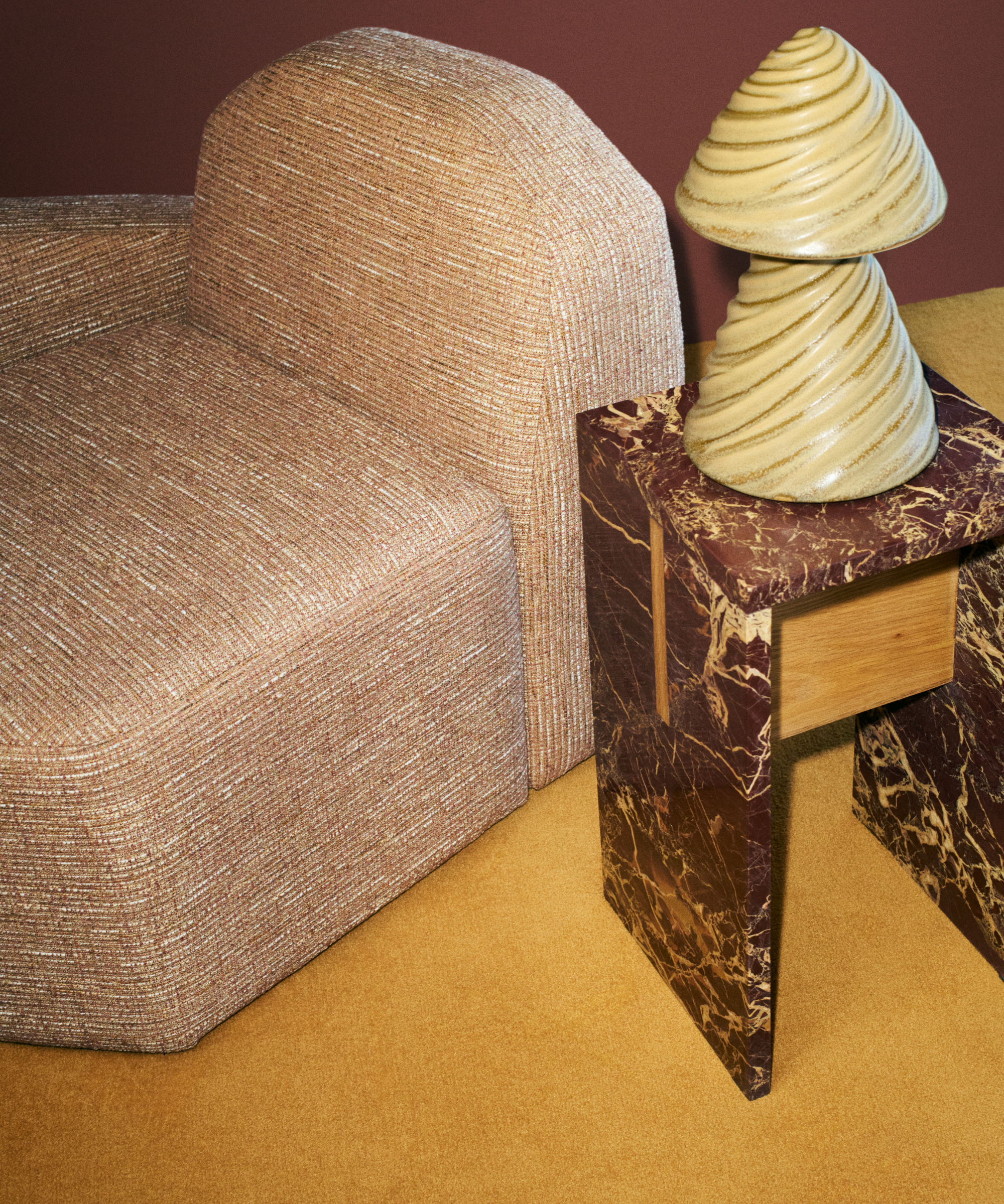 Kelly Wearstler x H&amp;amp;M Home modular sofa chair, marble side table, and sculptural table lamp pictured in a burgundy room with ochre carpet.