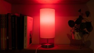 The Hive Smart Light Bulb tuned to red in a lamp on a shelf