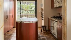 a small luxury kitchen with a red island and wood parquet flooring