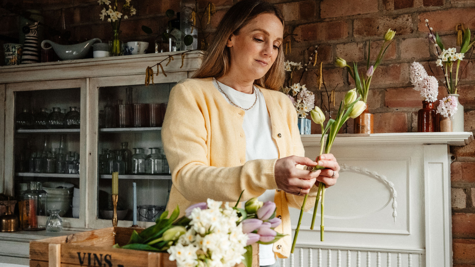 Woman in yellow cardigan holding tulips in floristry workshop setting
