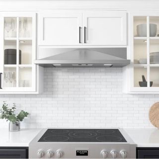A silver range hood in an all-white kitchen