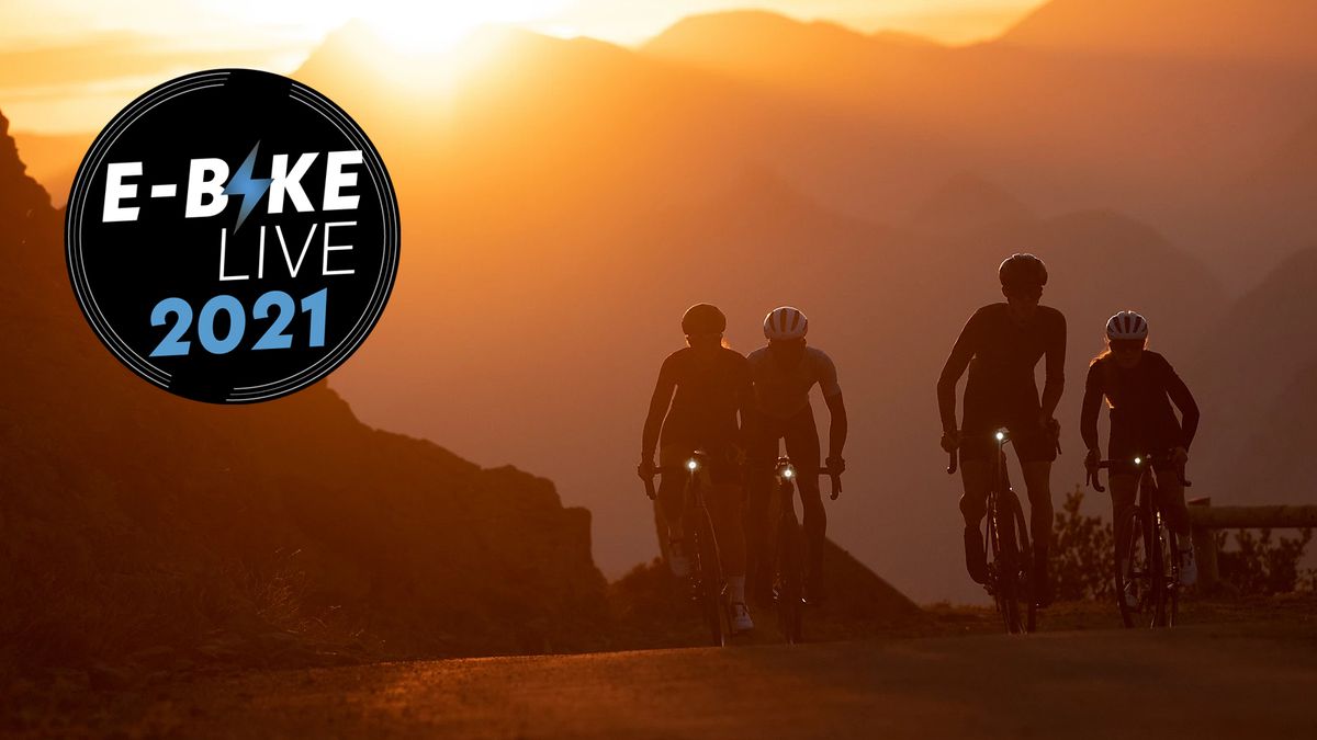 Four cyclists on electric bikes ride up a hill with a sunset behind