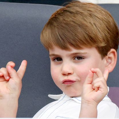 Prince Louis wears a white shirt and makes a funny face and poses with his hands