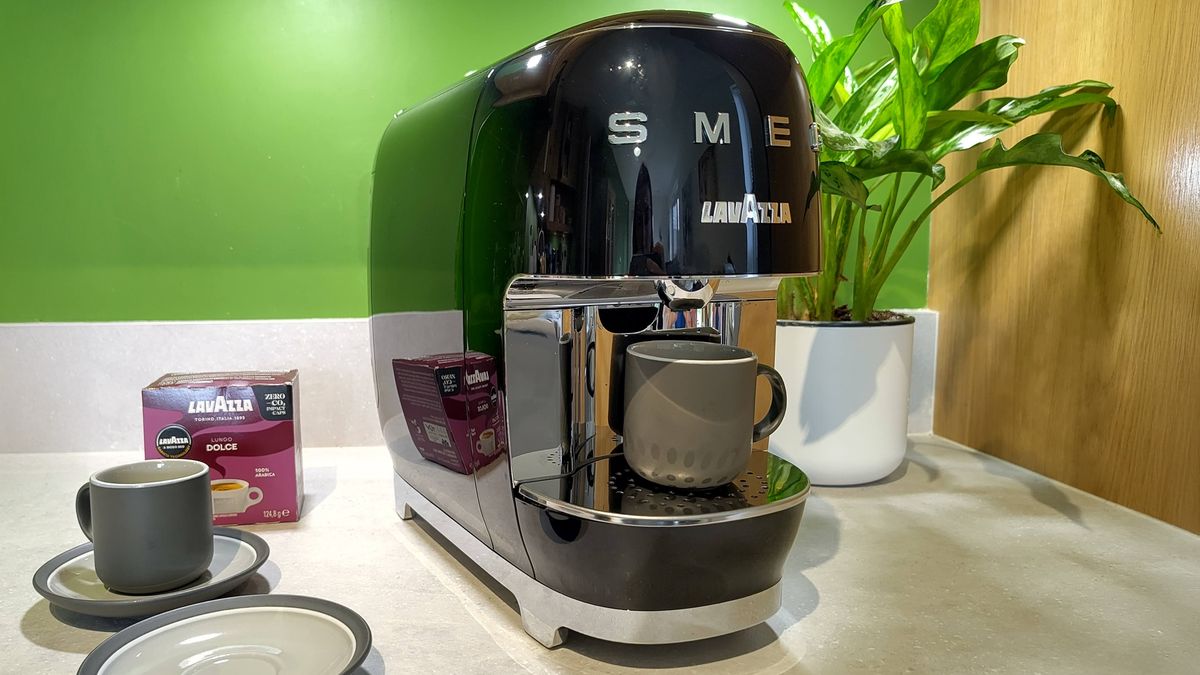 Lavazza A Modo Mio Smeg coffee maker on kitchen counter with espresso cups, box of coffee pods, and plant