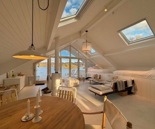 interior of boat house with white tongue and groove panelling, wooden table, white furniture, log burner and a variety of lighting