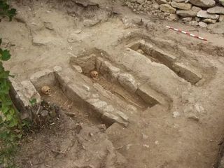 Uma foto mostrando três fossas funerárias retangulares com esqueletos dentro delas