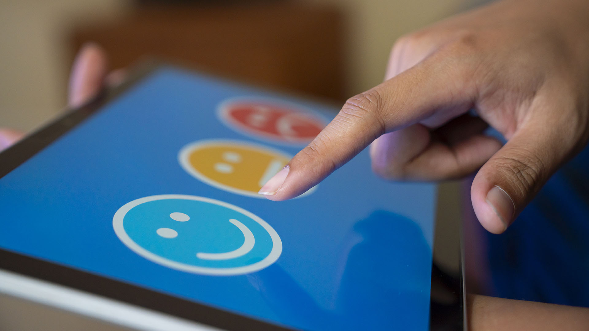 A finger about to press a smiley face on a tablet