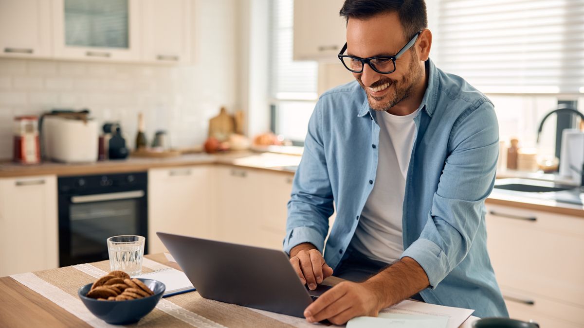 A man sitting at an island table in a kitchen and using a laptop