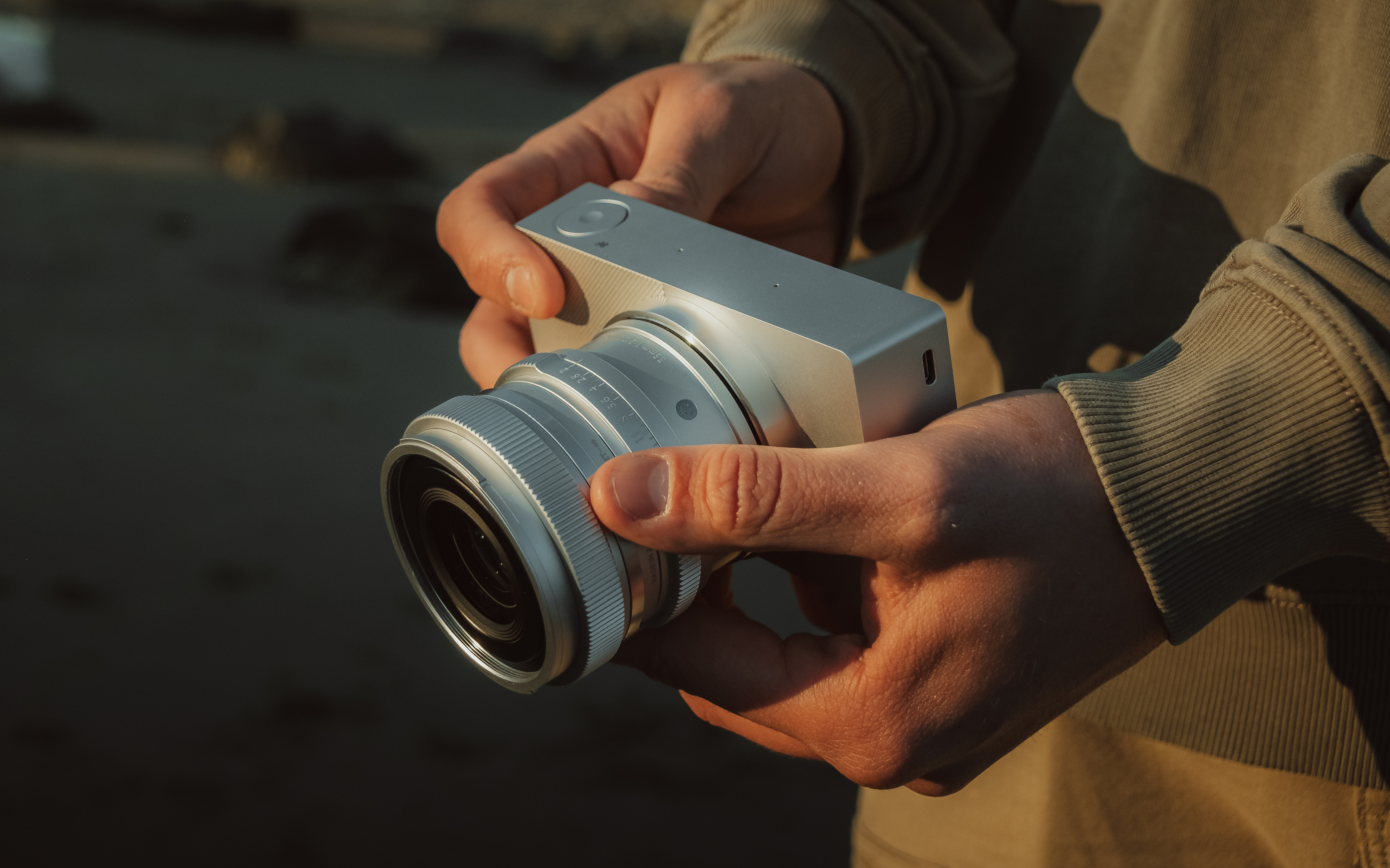 A person holding a sleek silver camera with a large lens, ready to capture a moment during a sunset on a beach.