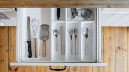 A good example to aspire to when learning how to declutter kitchen drawers. Image shows an open kitchen drawer with a cutlery divide and cutlery in a kitchen with a wooden floor and wooden counter tops