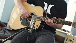 Man wearing black t-shirt records his acoustic guitar