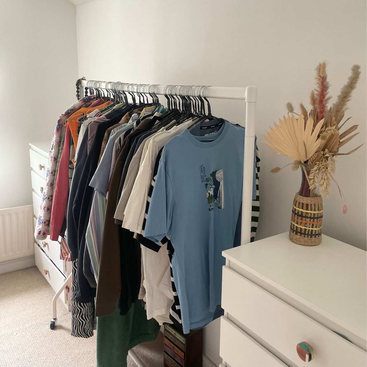 White painted bedroom with a clothes rail full of hanging clothes