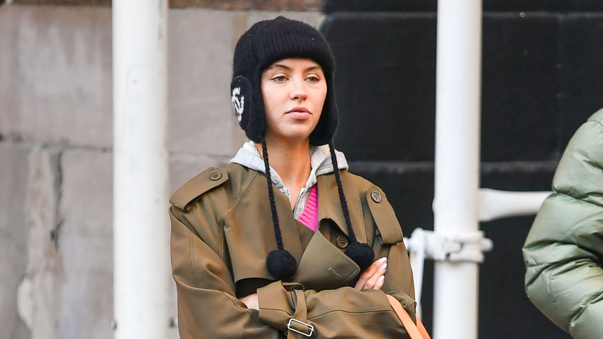 Iris Law wearing a black hat, trench coat, and red handbag