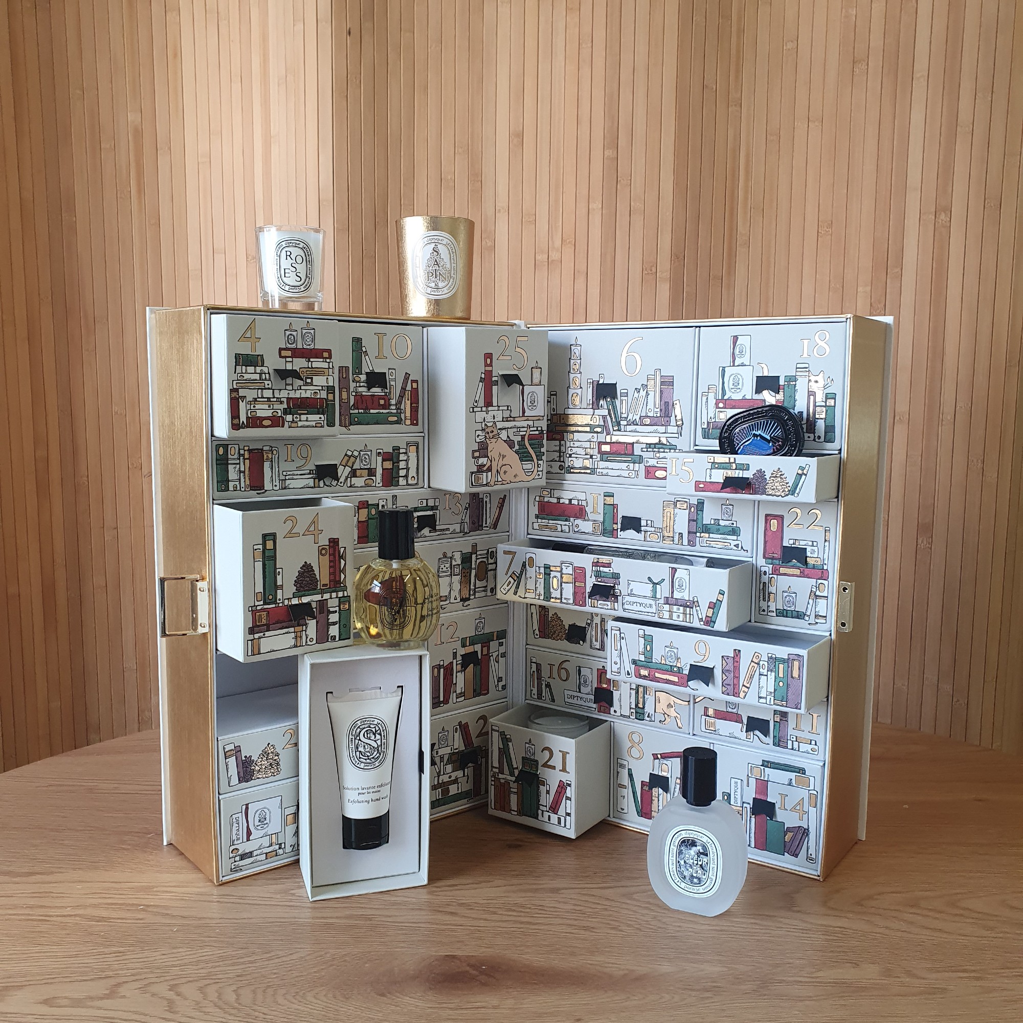 Diptyque advent calendar 2025 with open compartments on a wooden table with a panelled backdrop