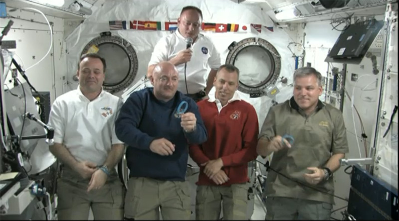 Space shuttle commander Mark Kelly shows his &quot;Peace, Love, Gabby&quot; blue rubber bracelet, which he wears to honor his wife, wounded Congresswoman Gabrielle Giffords. Kelly, in blue, is floating in the International Space Station with his fellow NASA astrona