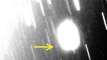 a black and white, blurry image with lots of white streaks. There is a white blob in the center-left to which a yellow arrow is pointing.