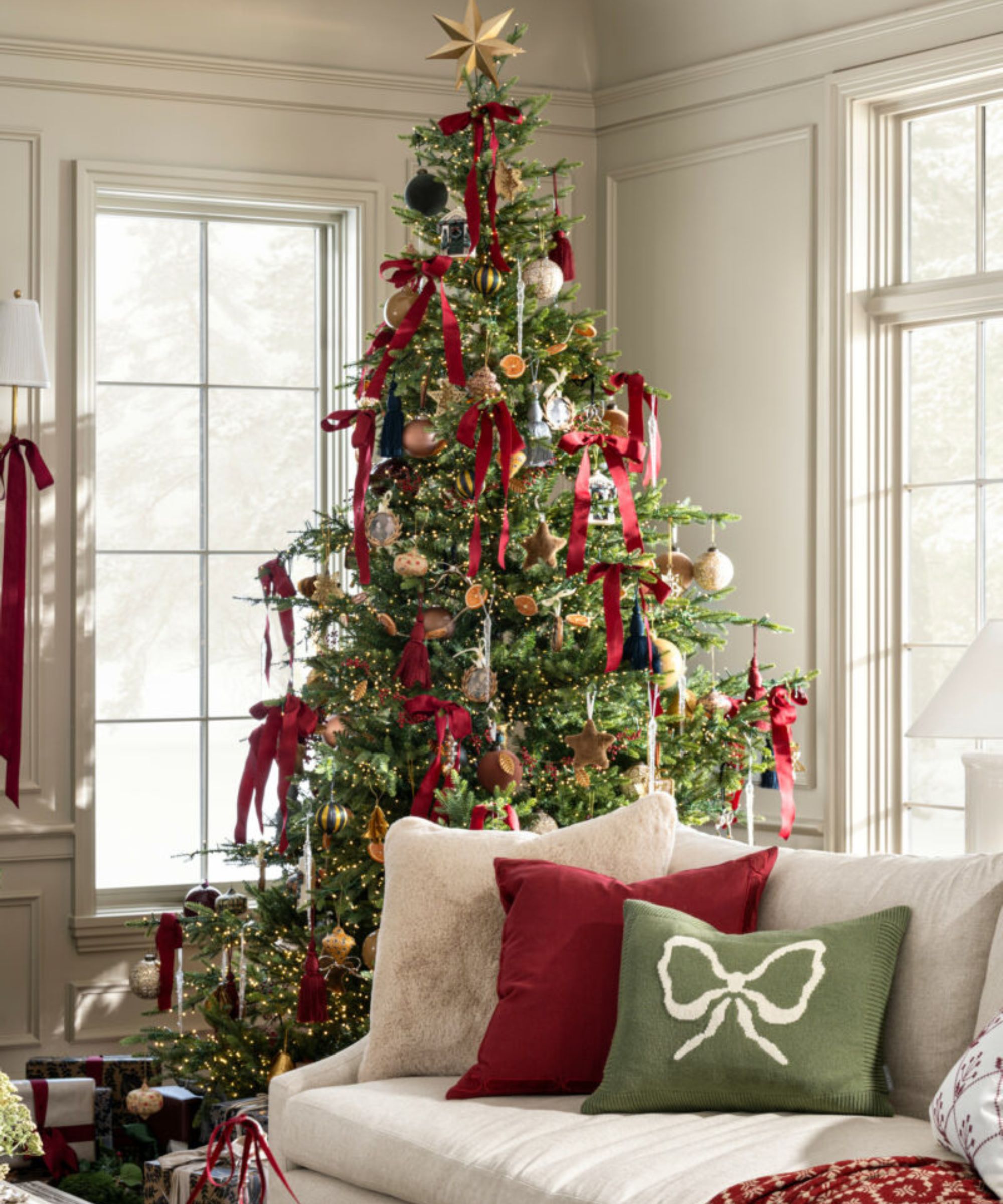 Living room with cream sofa, green and red cushions and a Christmas tree in the corner with a star topper and red bows