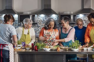 A group of mature women cooking together in a large kitchen.