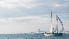 A white sailboat sails through Rhode Island's Newport Harbor on a clear day with the Newport Bridge in the background