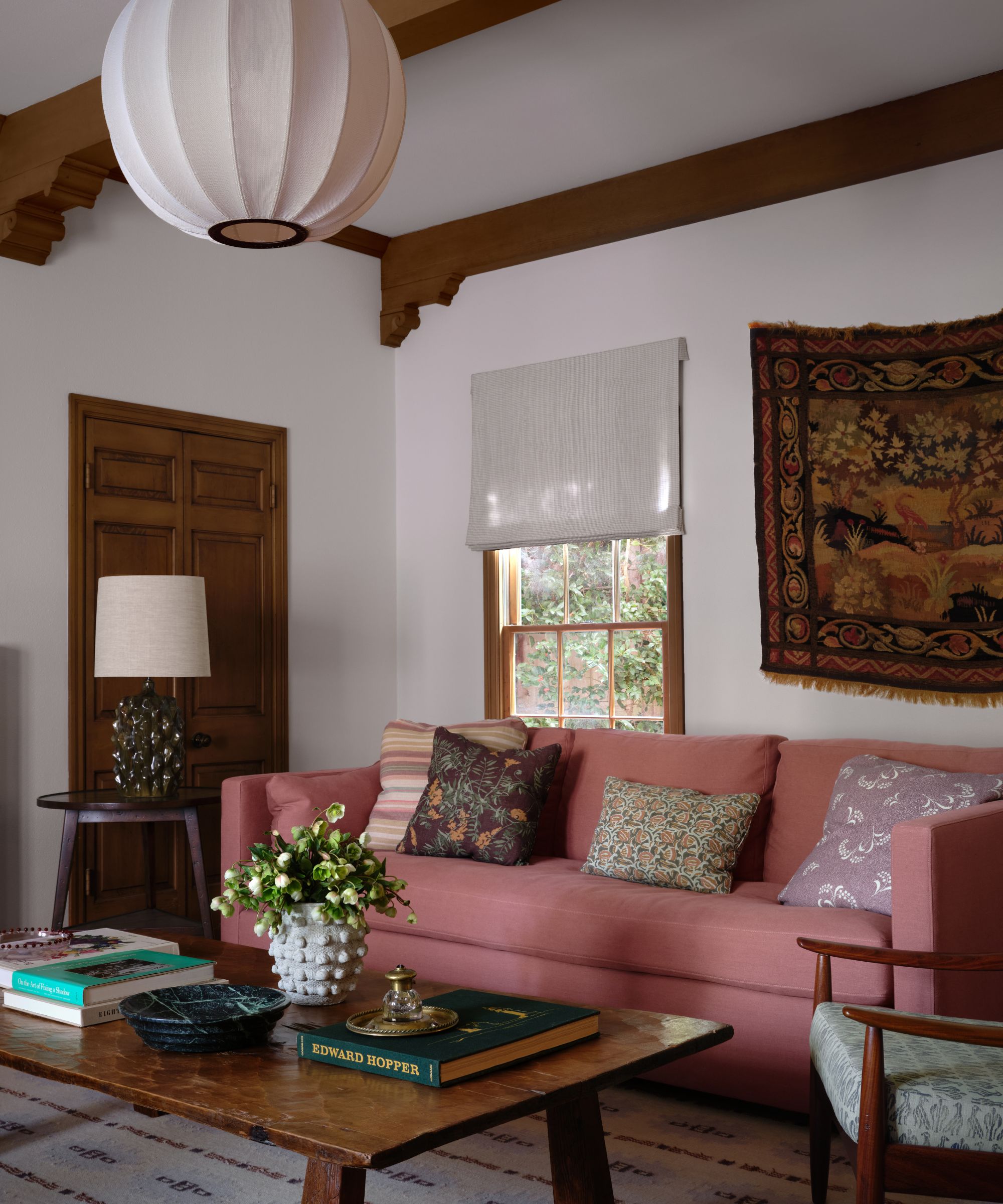 A warm living room featuring a dusty rose sofa, a rustic wooden coffee table with books, and a large white globe pendant light hanging from a beamed ceiling