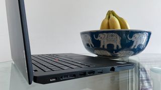 A side view of a Lenovo ThinkPad L14 sat on a clear glass table next to a bowl of bananas