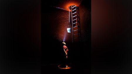 Man cleaning inside of empty wine vat looks up towards entrance of the vessel at the top of a ladder. A bucket hands via a rope from the entrance above.