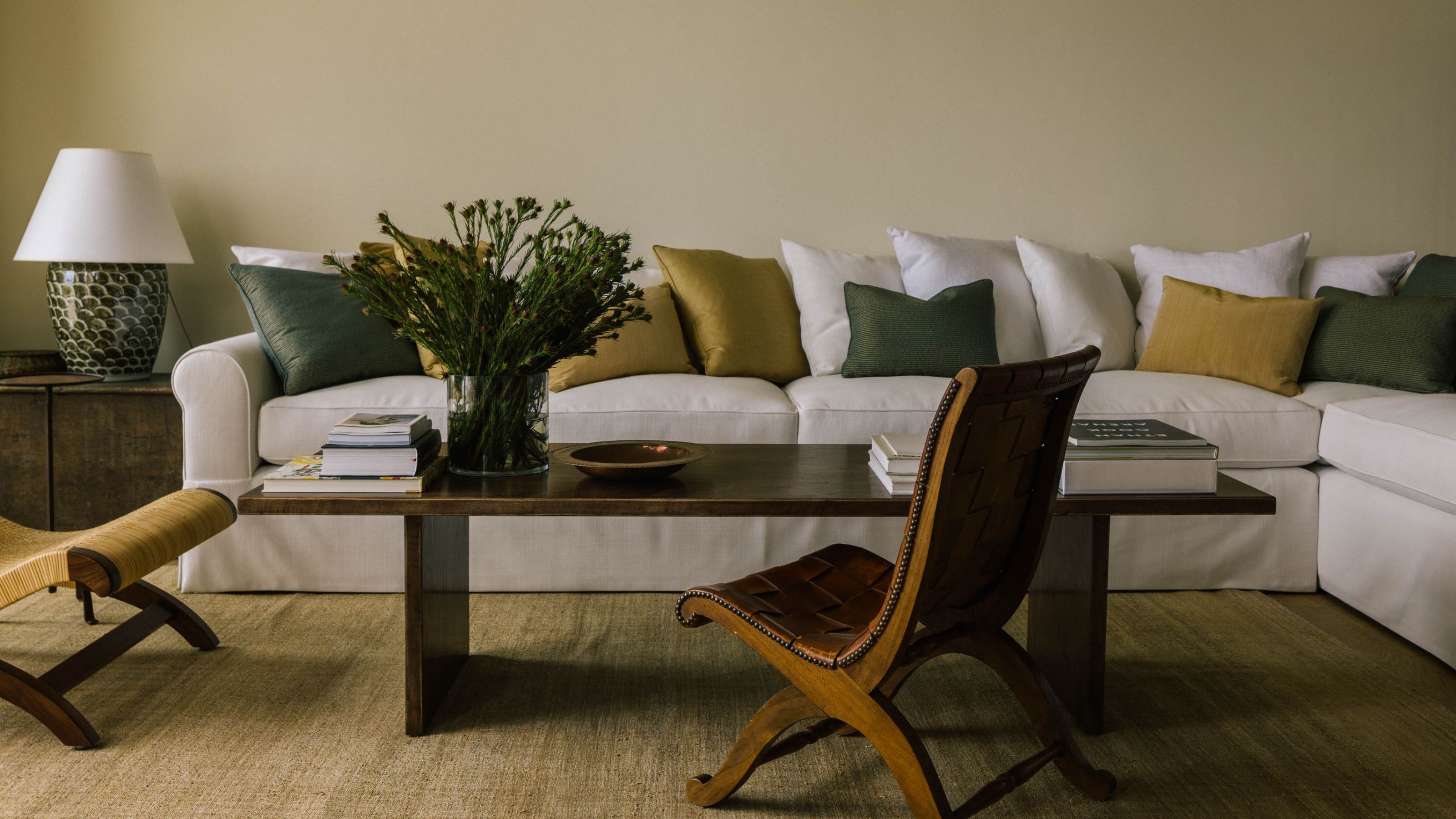 a neutral californian living room with a large white sectional styled with green and yellow throw pillows with a mix of Spanish-style vintage wooden furniture pieces