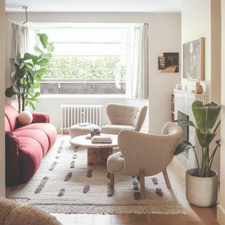 A living room with a red curved sofa and two boucle armchairs with a round stone coffee table in the middle