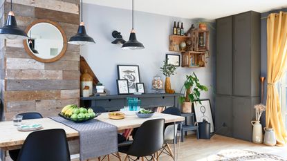 Spillett house: dining-living area with wood effect floor, wood dining table with metal pin legs, black Eames-style chairs, grey built-in storage and black pendants