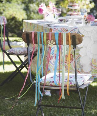 A wooden outdoor chair back decorated with multi colored ribbon ties