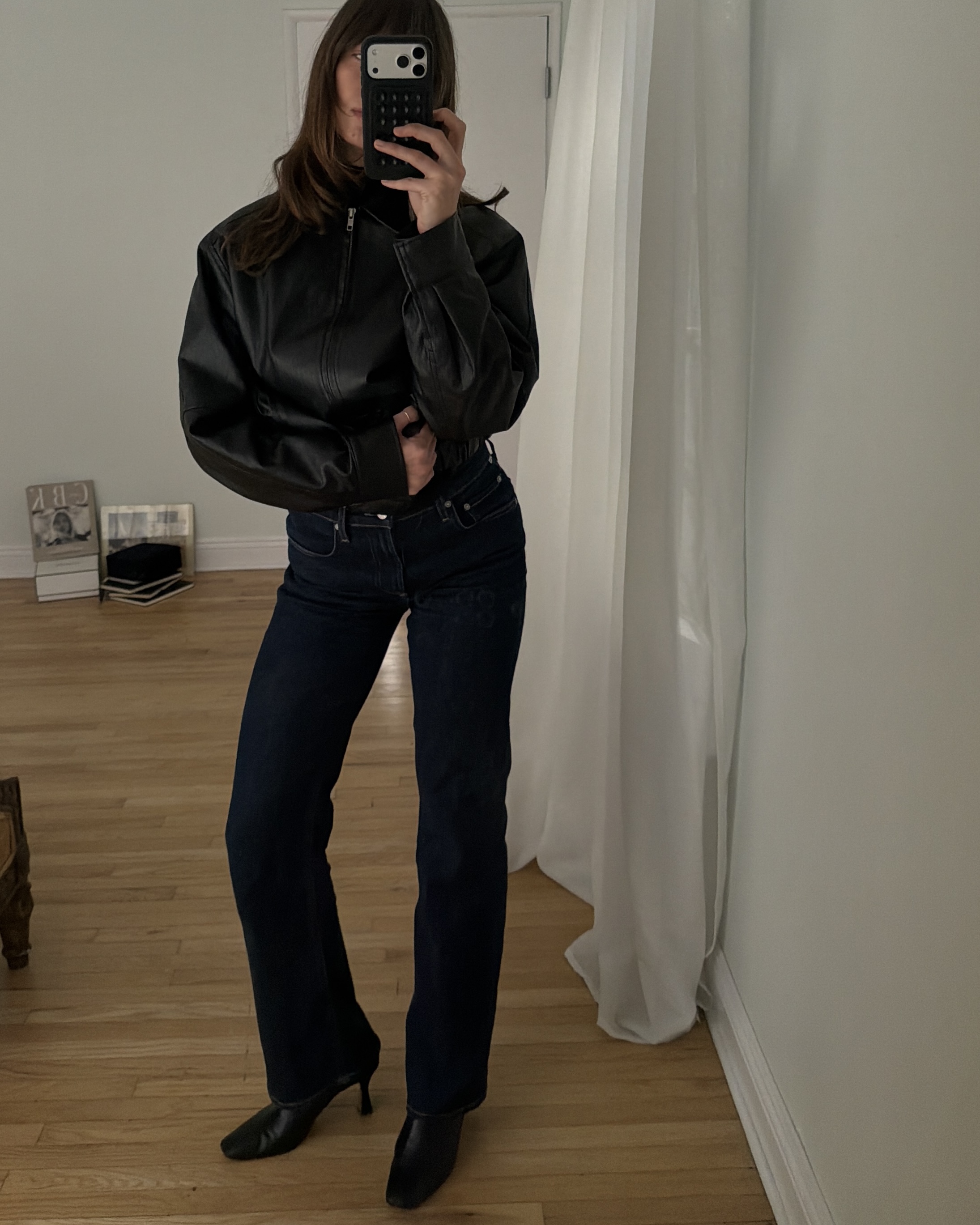 Kathryn Zahorak posing in mirror wearing leather jacket, dark wash jeans, and black boots