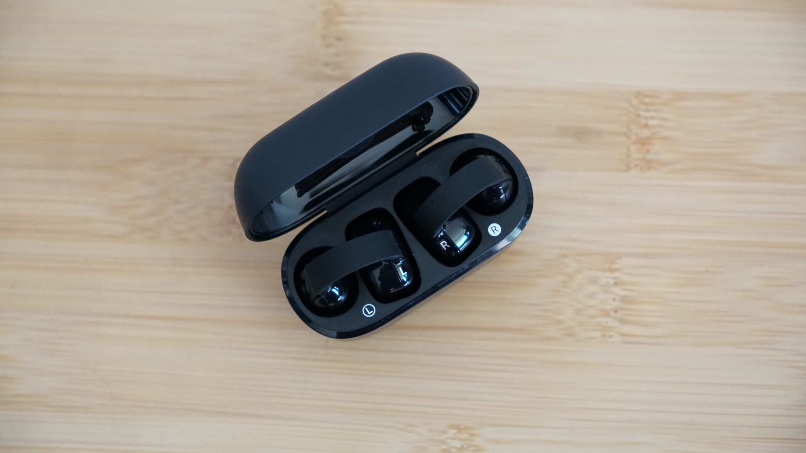 Sennheiser's Accentum Clip held in a hand, over a wooden table, with the case visible