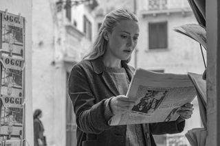 a woman (Dakota Fanning as Marge Sherwood) reads a newspaper while standing outside, in 'ripley'