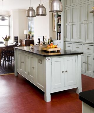 A kitchen with a red ochre vinyl floor and pale grey-green island and cabinets