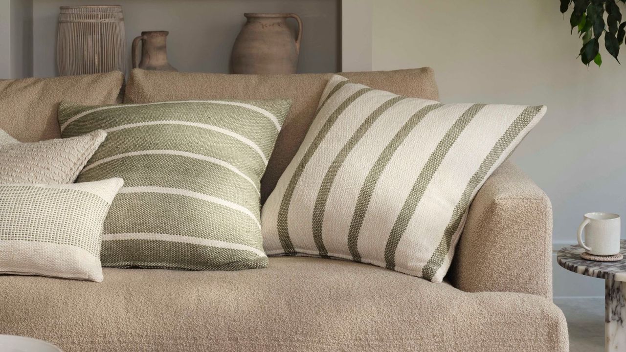 A beige boucle sofa with cream and green striped thro pillows in a neutral living room.