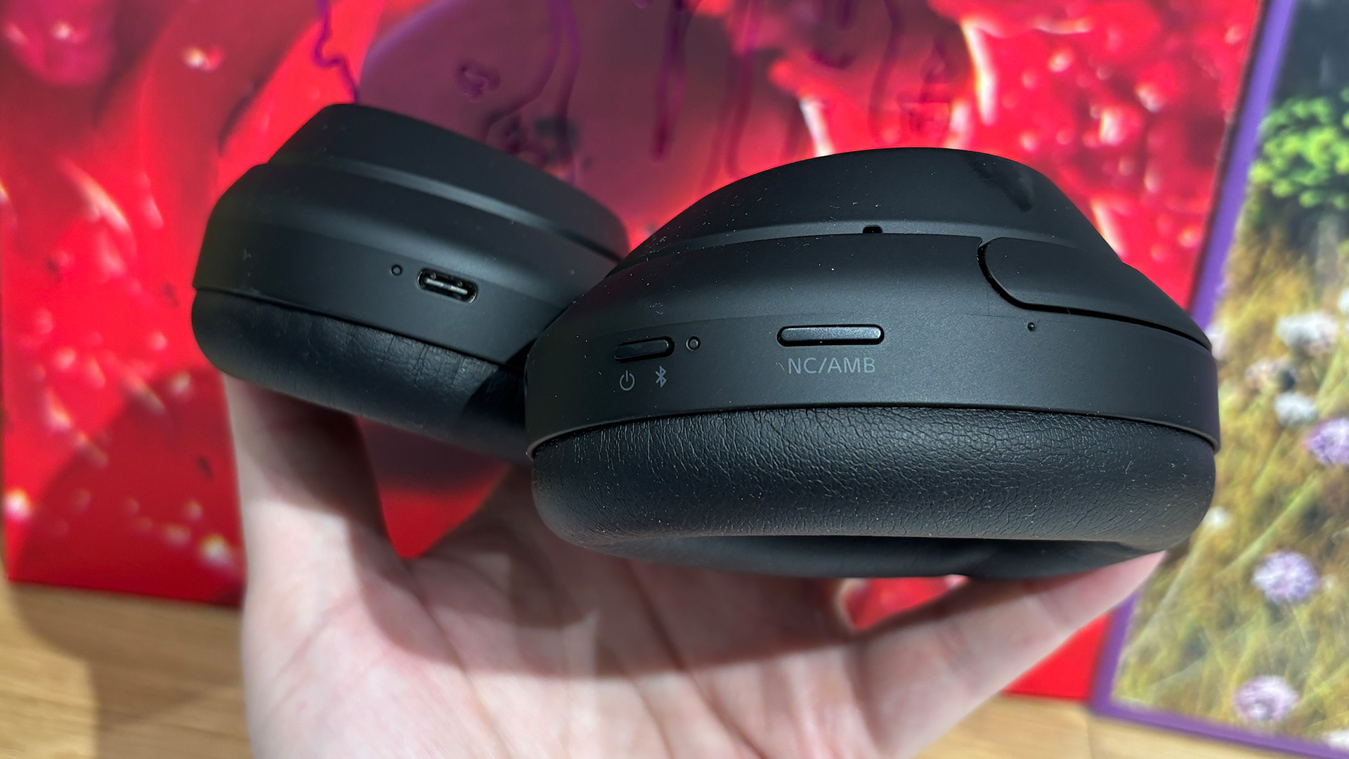 Sony WH-1000XM4C over-ear headphones held in hand in front of busy bookshelf