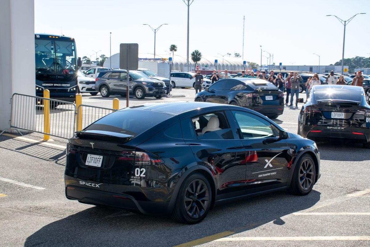 astronauts walk out of a building and board black cars.