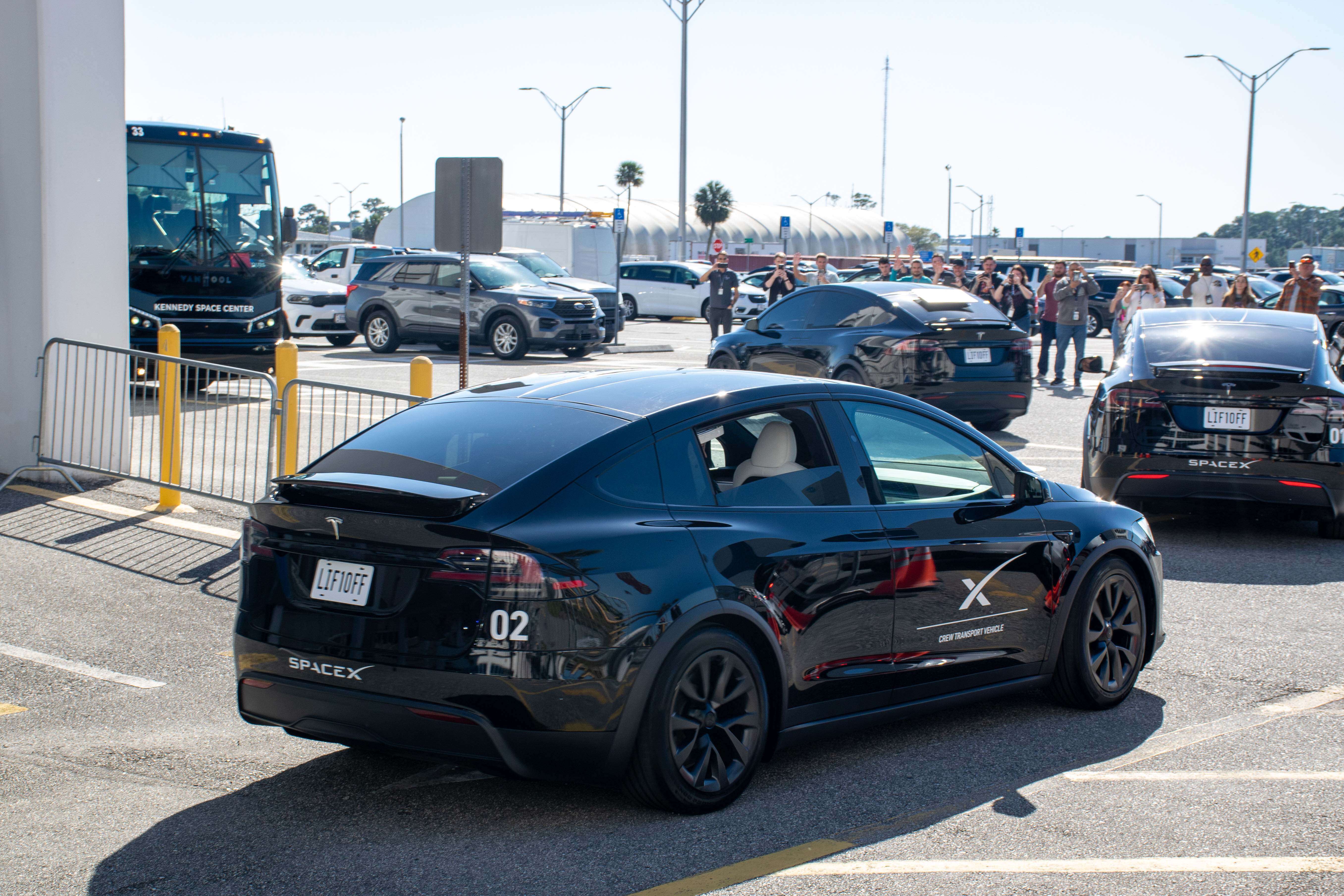 astronauts walk out of a building and board black cars.