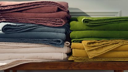 Five Brooklinen Washed Velvet Quilts in every color folded up on a wooden bench.