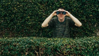 Guy in hedges with binoculars