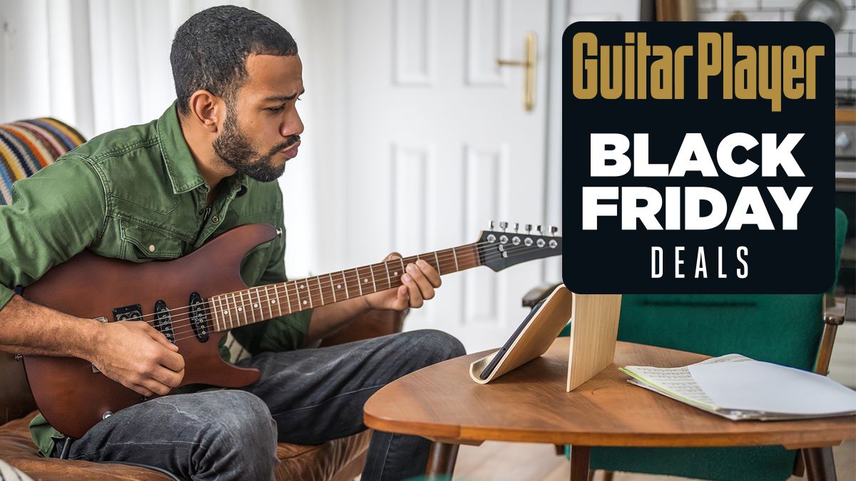 Man playing brown guitar watches a lesson on a tablet