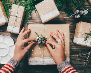 Woman finishing Christmas gift wrapping with a pine cone