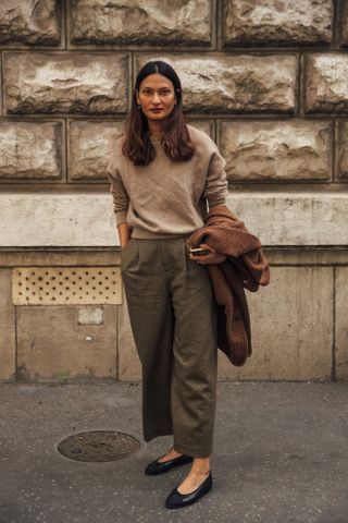 A guest attends paris fashion weeks spring summer 2025 wearing a beige sweater with grey trousers and black ballet flats