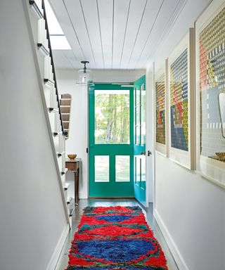 white hall with green door, red patterned rug and colorful artwork