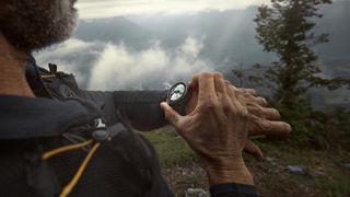 A photo of a man in the mountains wearing a Garmin Fenix 8 Pro, using it to check his nearby mapped location.
